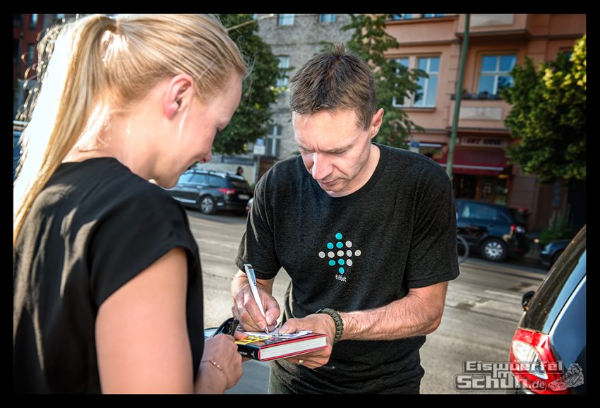 Jens Voigt signiert sein Buch Shut Up Legs für Nadin von eiswuerfelimschuh. Beide stehen auf einer Straße in Berlin Mitte.