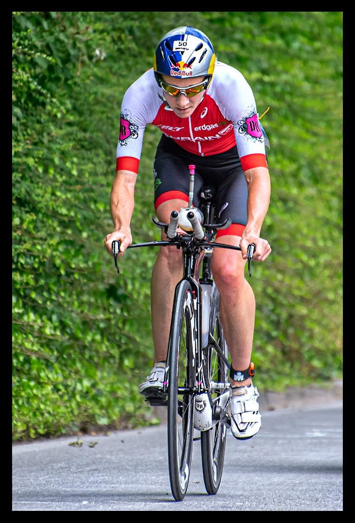 Daniela Ryf Ironman Radstrecke roter tri-suit aero helm red-bull logo zeitfahrrad felt schwarz anstieg vor wand mit pflanzen sommerlich