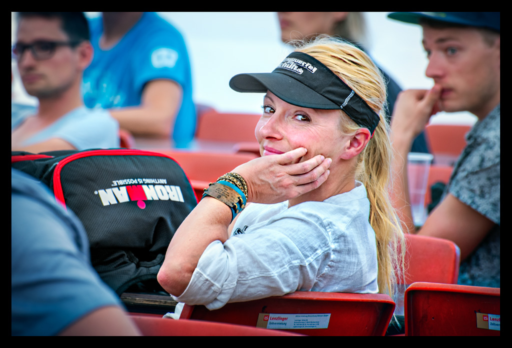 ironman triathletin bei wettkampf besprechung race briefing blickt in kamera lächelt weiße bluse blonder pferdeschwanz rucksack M logo