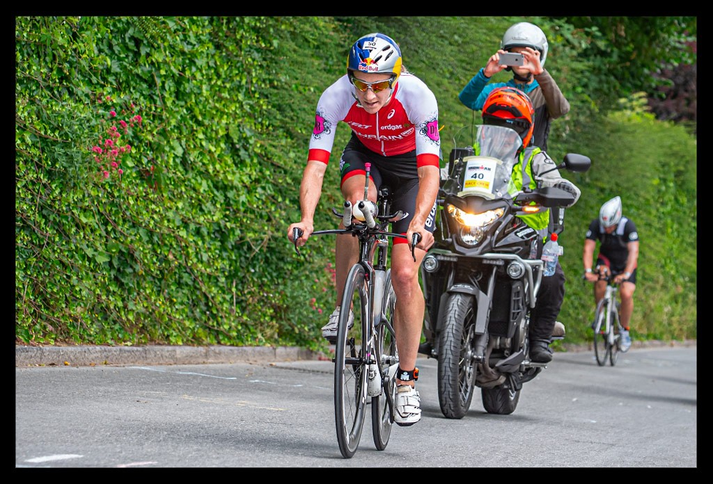 Daniela Ryf Ironman anstieg Radstrecke heartbreak hill roter tri-suit aero helm red-bull logo zeitfahrrad felt schwarz anstieg vor wand mit pflanzen sommerlich motoräder kameras tv live