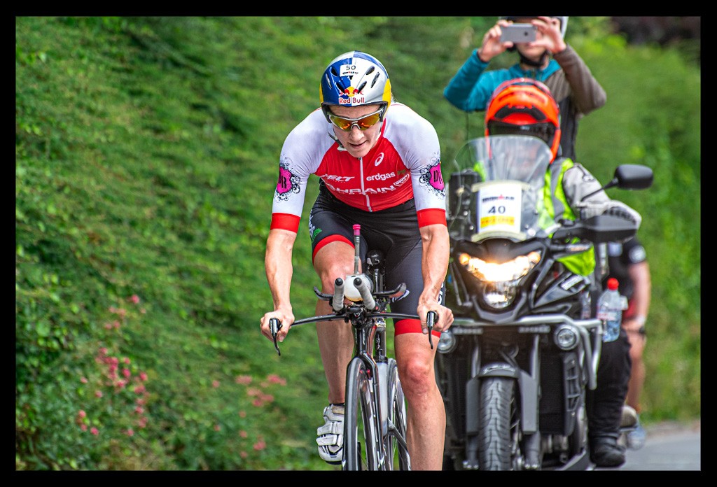 Daniela Ryf Ironman Radstrecke heartbreak hill berg anstieg roter tri-suit aero helm red-bull logo zeitfahrrad felt schwarz anstieg vor wand mit pflanzen sommerlich motoräder kameras tv live