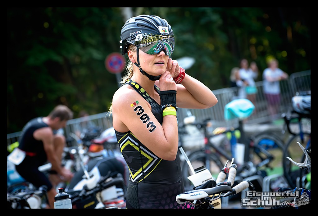 Athletin Nadin beim BerlinMan Triathlon in Wechselzone schließt ihren Helm. Hintergrund Athleten und Fahrräder.