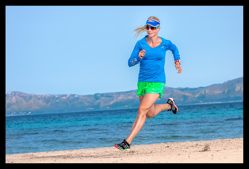 Frau beim Lauftraining am Strand mit Mittelmeer im Hintergrund auf Mallorca mit kurzer Laufhose und Laufshirt