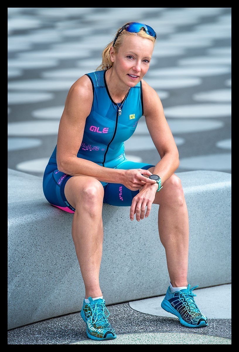Triathletin sitzt auf Stufe im TriSuit lächelnd und betätigt Multisportuhr