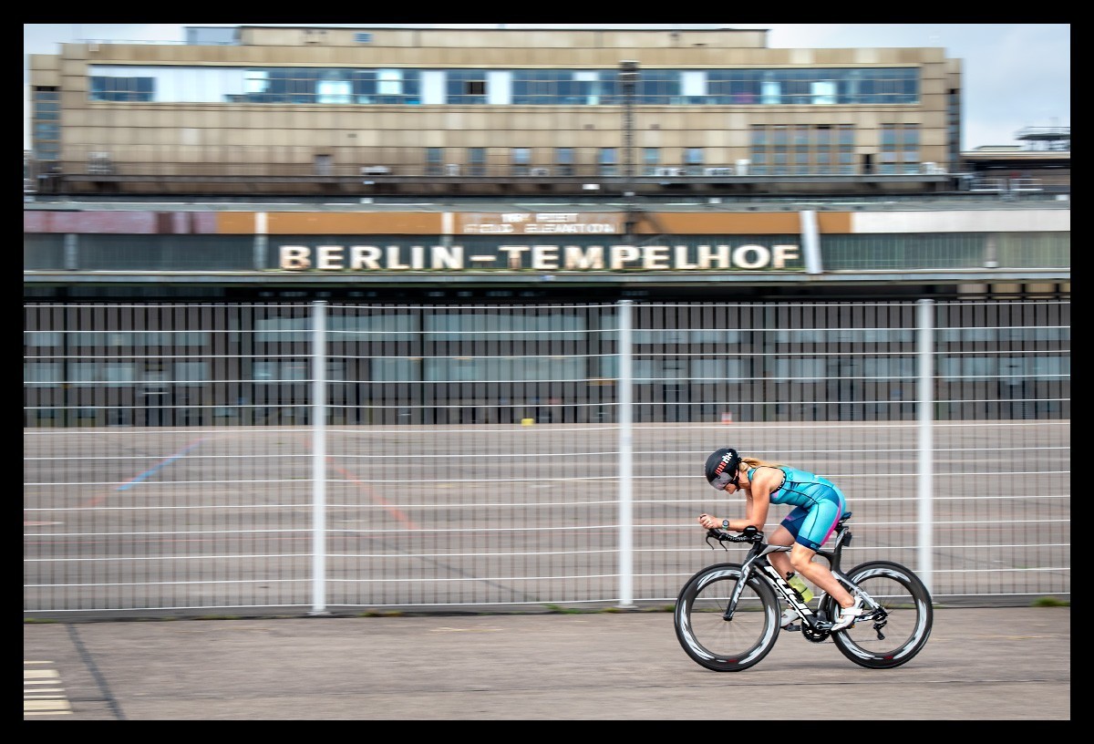 Athletin fährt mit einem Zeitfahrrad. Sie trägt einen Tri-Suit von ALE in Hellblau mit der Garmin Forerunner 745 Multisportuhr. Tempelfhofer-Flugfeld-Flughafen in Berlin. Produkttest. Review.