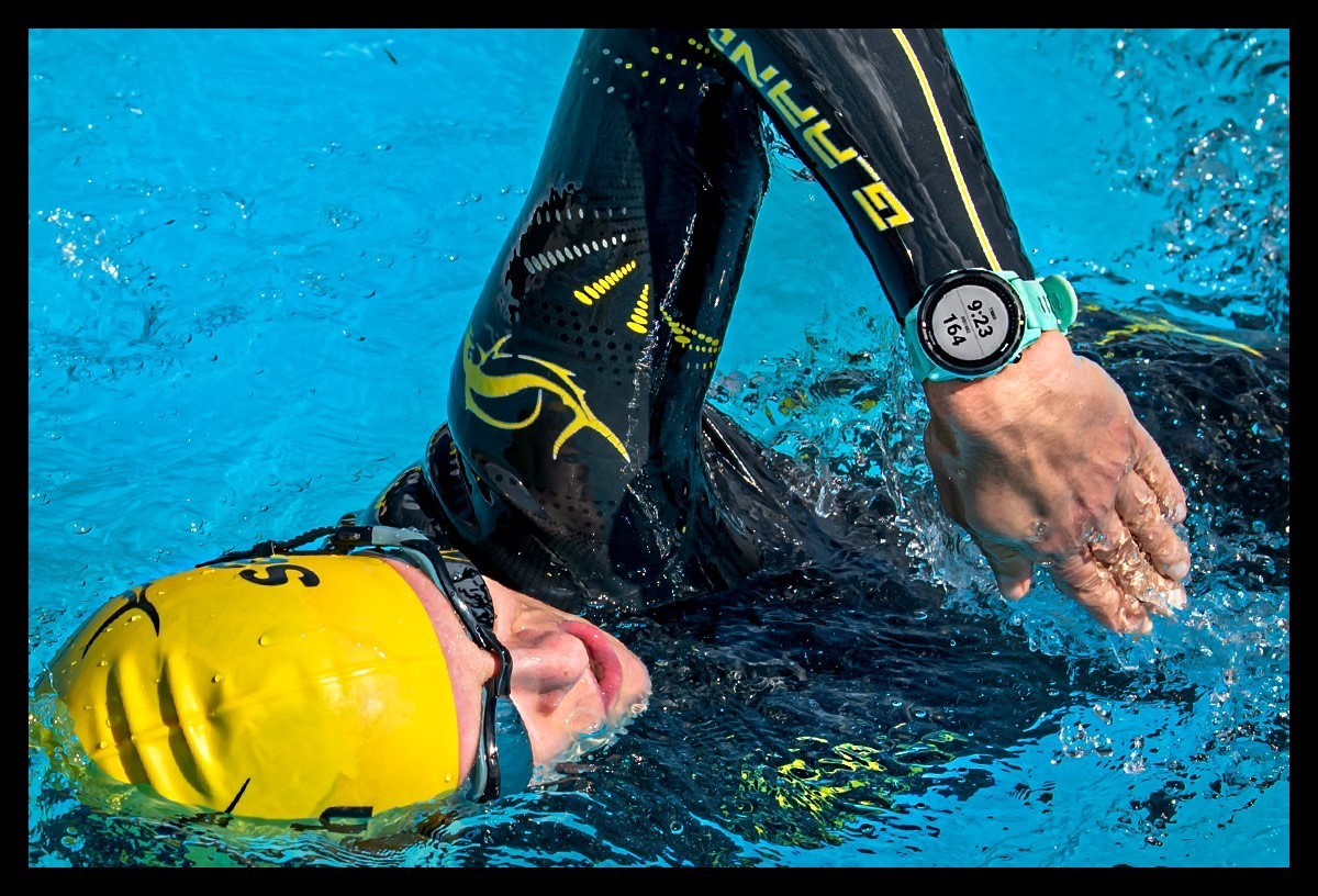 Triathletin schwimmt im blauem Wasser. Sie trägt einen Neoprenanzug von Sailfish, gelbe Badekappe, Schwimmbrille und Garmin Forerunner 745 Multisportuhr. Detaillierte Nahaufnahme. Produkttest. Review.