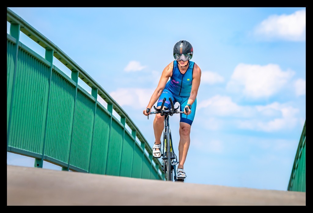 Auf Brücke Triathletin auf Zeitfahrrad mit Aero Helm und Tri Suit