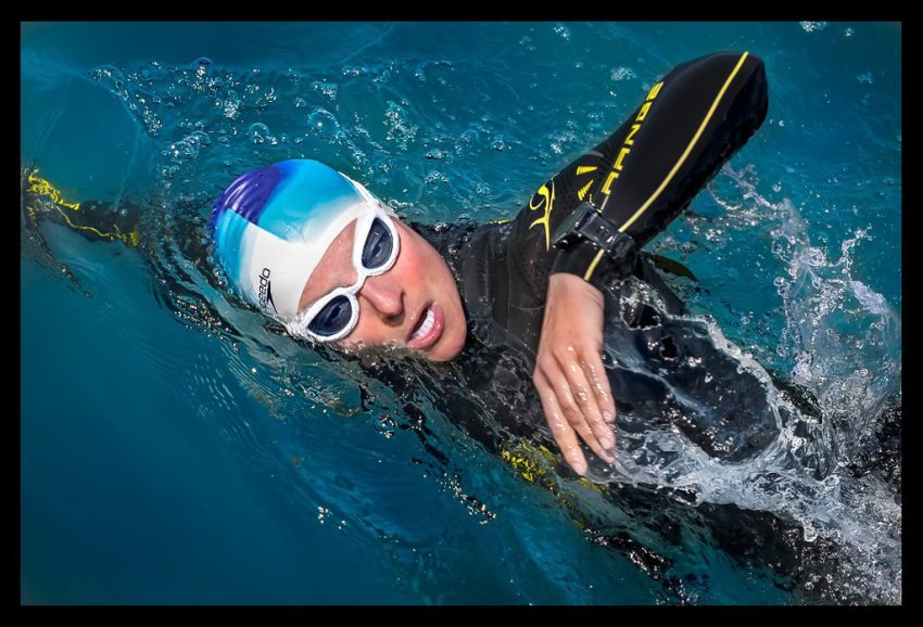 Triathletin beim Schwimmtraining im offenen Gewässer Portrait mit Neoprenanzug, Schwimmbrille, Badekappe und GPS Sportuhr