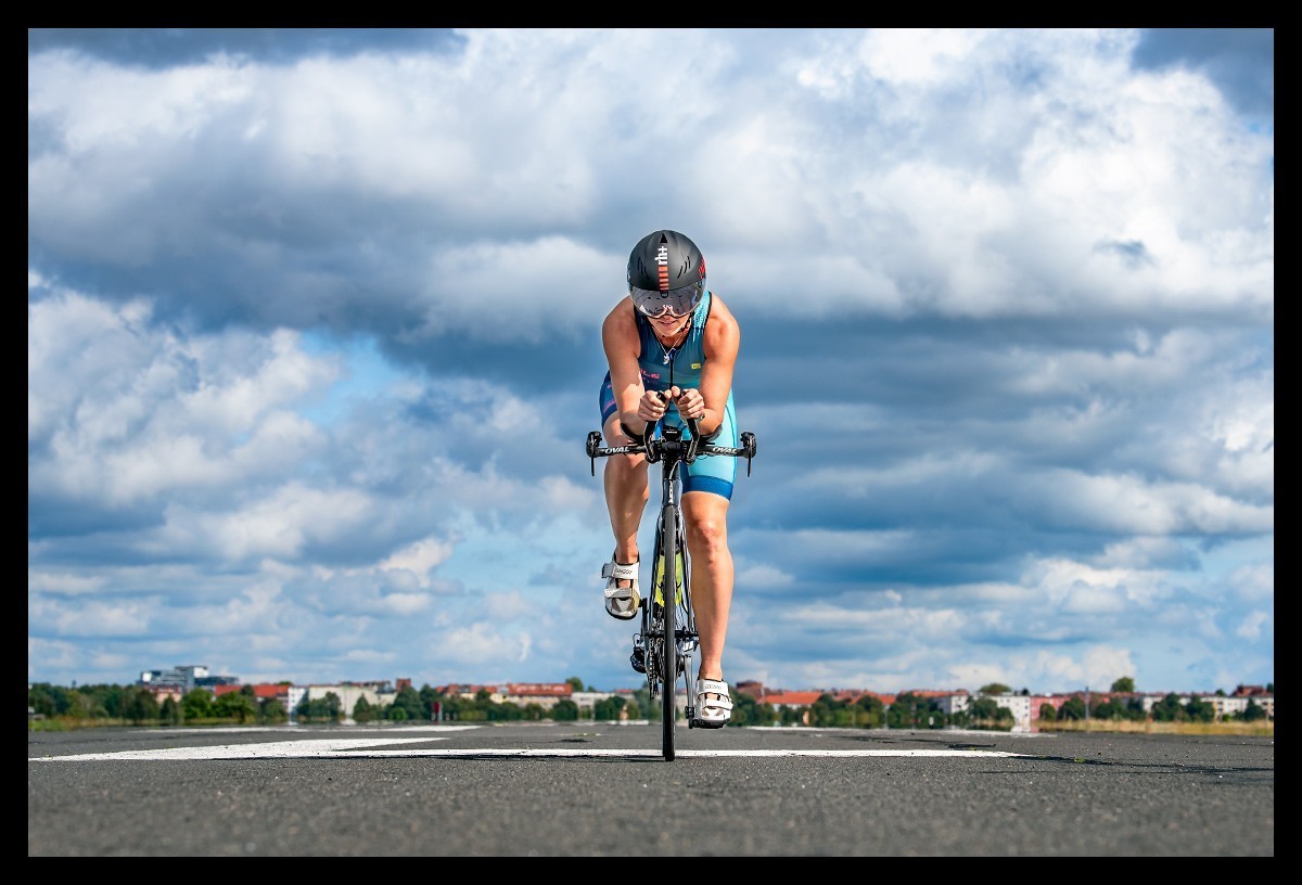 Triathletin beim Radtraining auf dem Tempelhofer Feld mit Garmin Edge 1030 Plus im Tri Suit und mit Zeitfahrrad Dramatischer Himmel