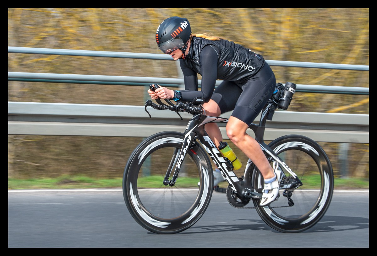 Radsportlerin auf Zeitfahrrad mit schwarzer Bekleidung und Helm und Garmin Rally Wattmesser Powermeter Sportfotografie