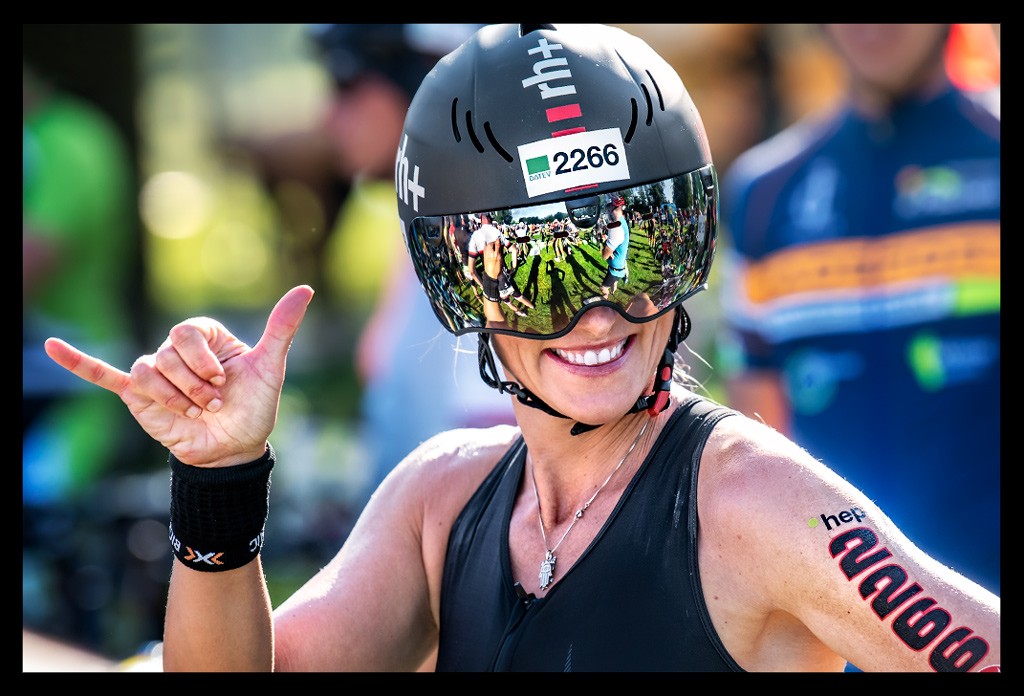 Challenge Roth Triathlon Staffel Bloggerin und Triathletin Nadin auf Radstrecke mit Trisuit und Helm macht Aloa Hang Loose Zeichen mit Hand