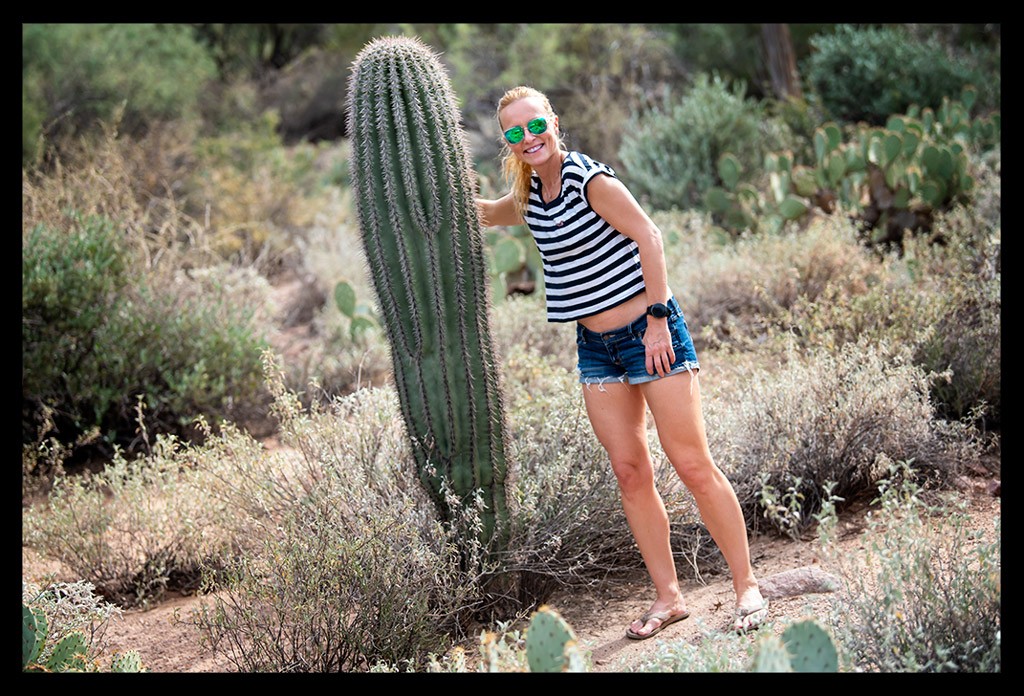frau in hotpants und riesiger kaktus wüste arizona sommerlich warm posiert shirt bauchfrei lächelt