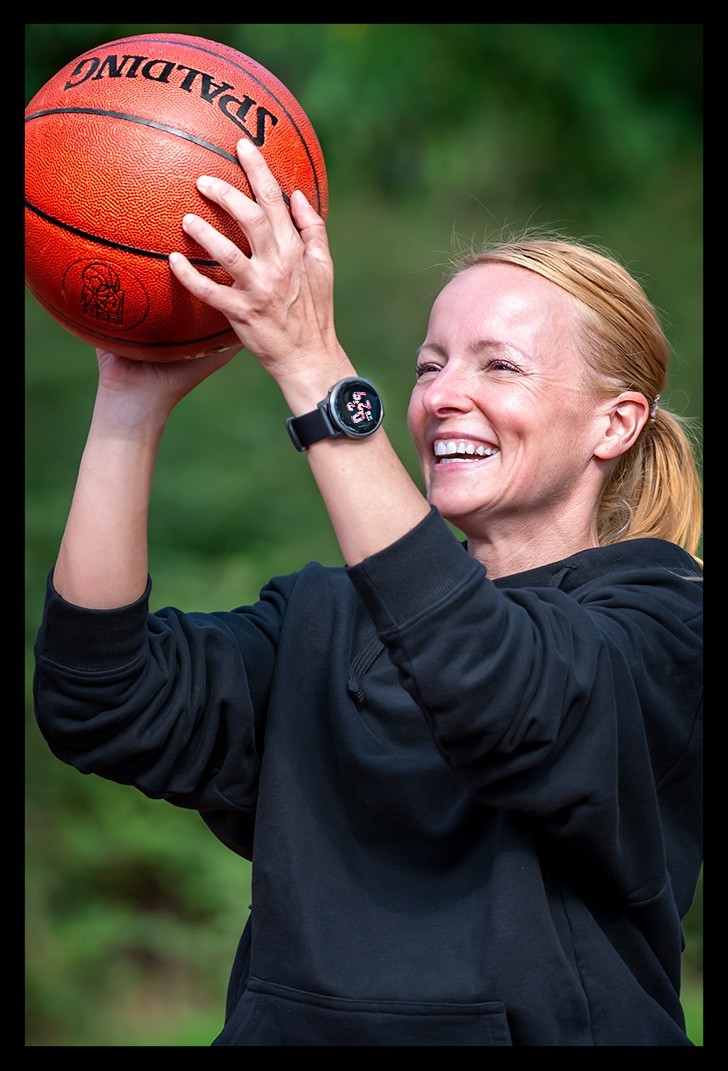 Frau mit Basketball in Hand Pferdeschwanz lächelt beim werfen mit Garmin Smartwatch im sommer licht
