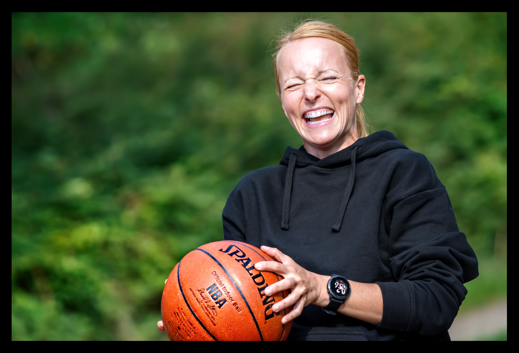 Frau mit Basketball in Hand Pferdeschwanz lächelt beim werfen mit Garmin Smartwatch im sommer licht