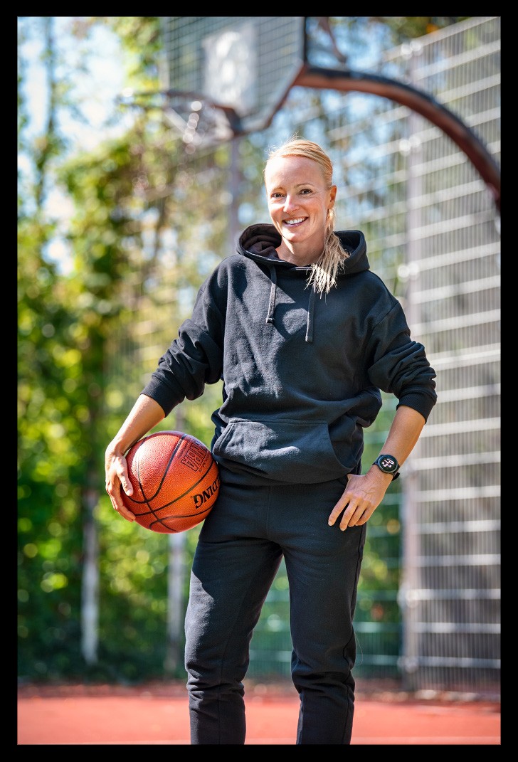 Nadin von eiswuerfelimschuh.de testet die neue Garmin beim Basketball. Schwarzer Anzug mit Ball in der Hand und Korb im Hintergrund.
