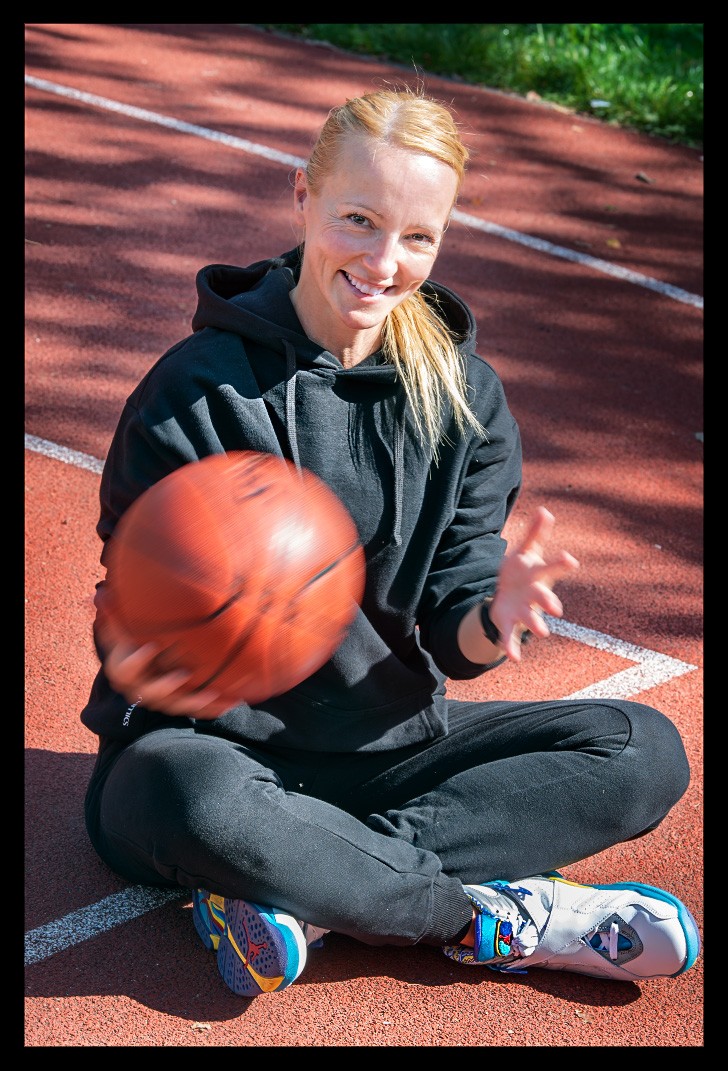 frau sitzt auf basketball court air jordan schuhe ball in hand posiert sonne im gesicht entpannt schwarzes outfit garmin uhr analyse training