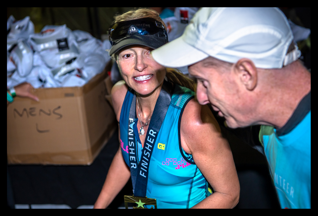 Nadin im Ziel Ironman Arizona Tempe Phoenix USA nach erfolgreicher Langdistanz mit lächeln im Gesicht und Helfer an der Seite mit Medaille um den Hals