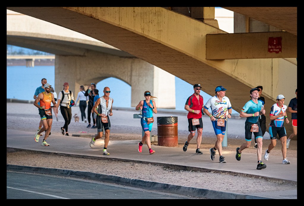 Nadin, Bloggerin und Triathletin von eiswuerfelimschuh.de beim Ironman in Tempe Arizona USA auf der Laufstrecke. Blaue Tri-Suit von ALE und sonnenbrille auf dem Kopf. Garmin Forerunner am Handgelenck. läuft unter Brücke hindurch mit anderen Triathleten