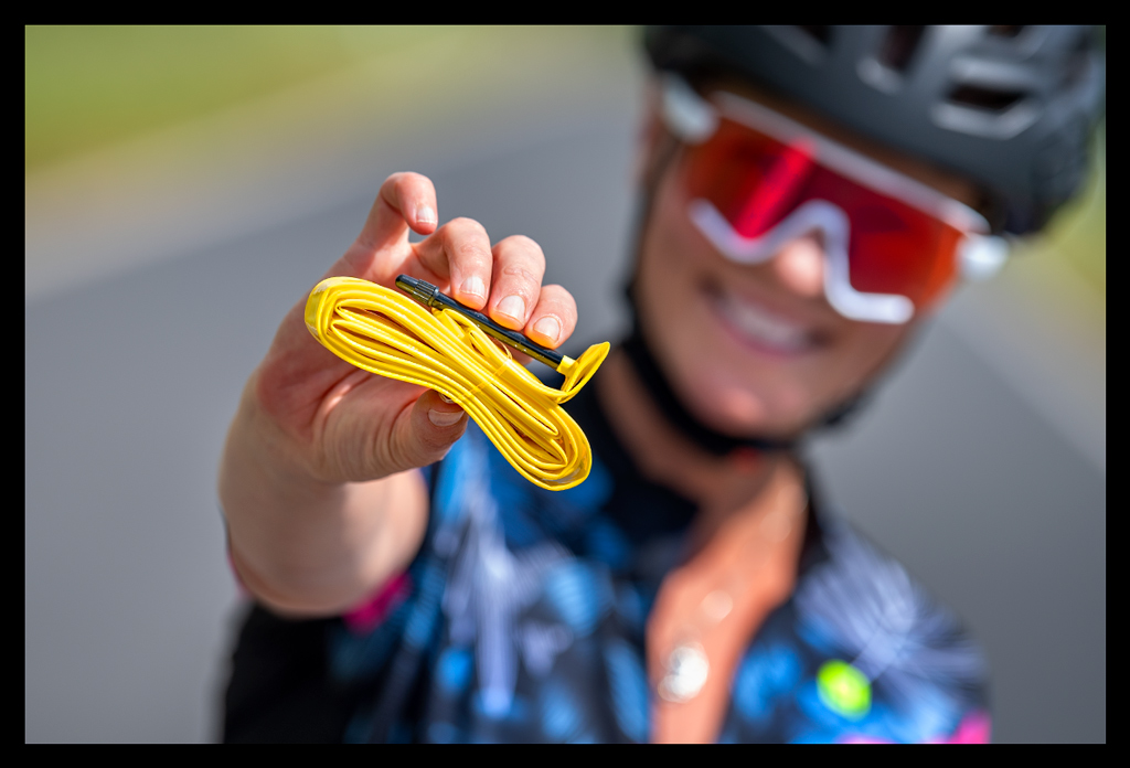 Frau hält Pirelli P-Zero Smartube gelb schlauch langes ventil in kamera radsportlerin helm sonnenbrille lächelt landstraße sommerlich trikot geöffnet halskette funkelt