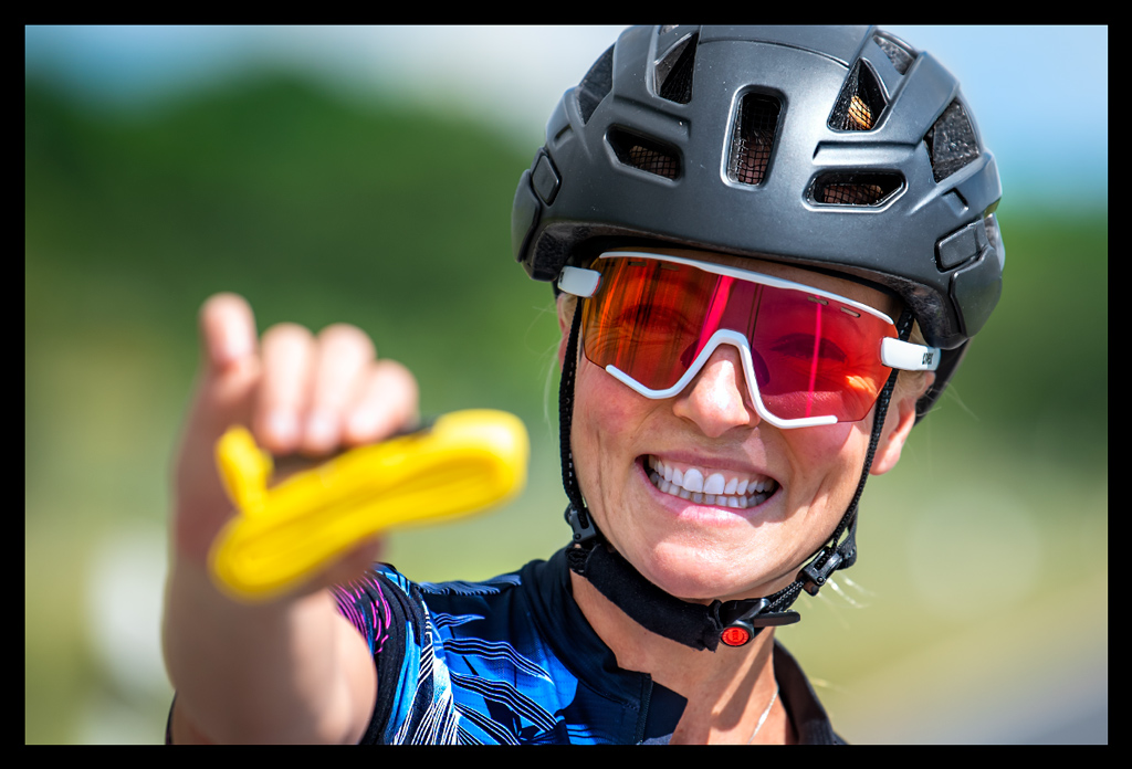 Frau hält Pirelli P-Zero Smartube gelb schlauch in kamera nahaufnahme radsportlerin helm sonnenbrille UVEX lächelt landstraße sommerlich trikot geöffnet halskette funkelt