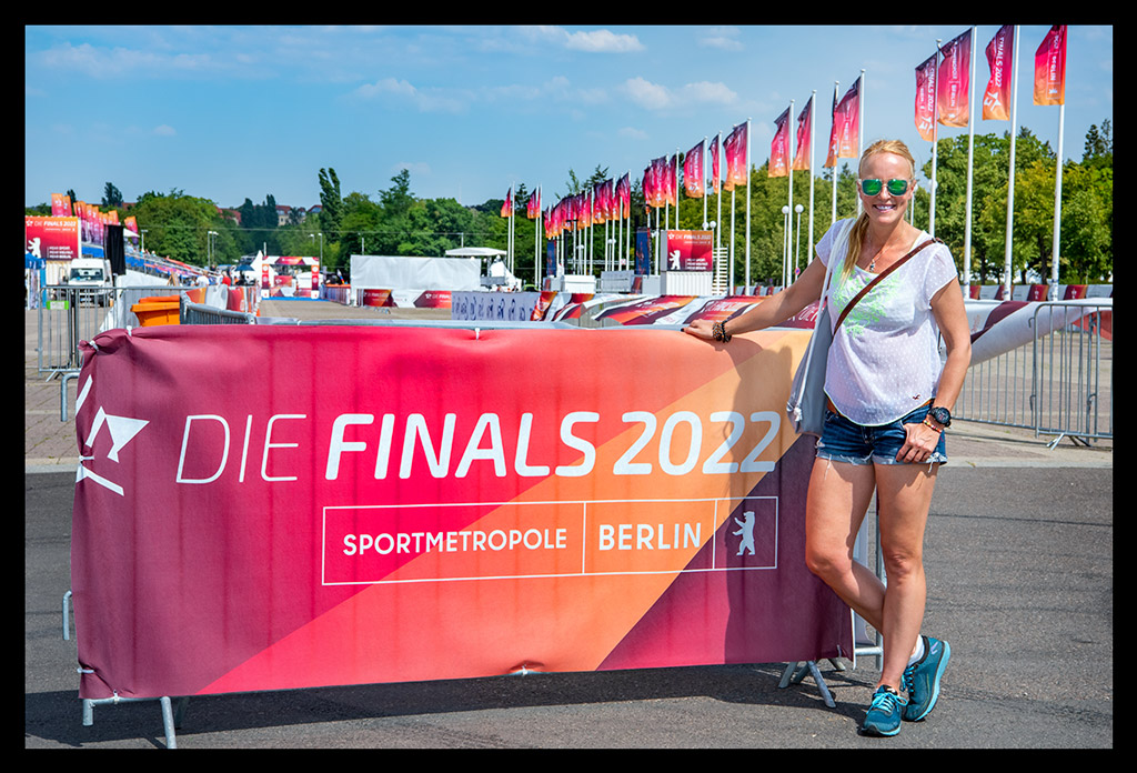 frau steht vor werbewand die finals 2022 sportmetropole berlin olympischer platz posiert lächelt flaggen im wind sommerlich
