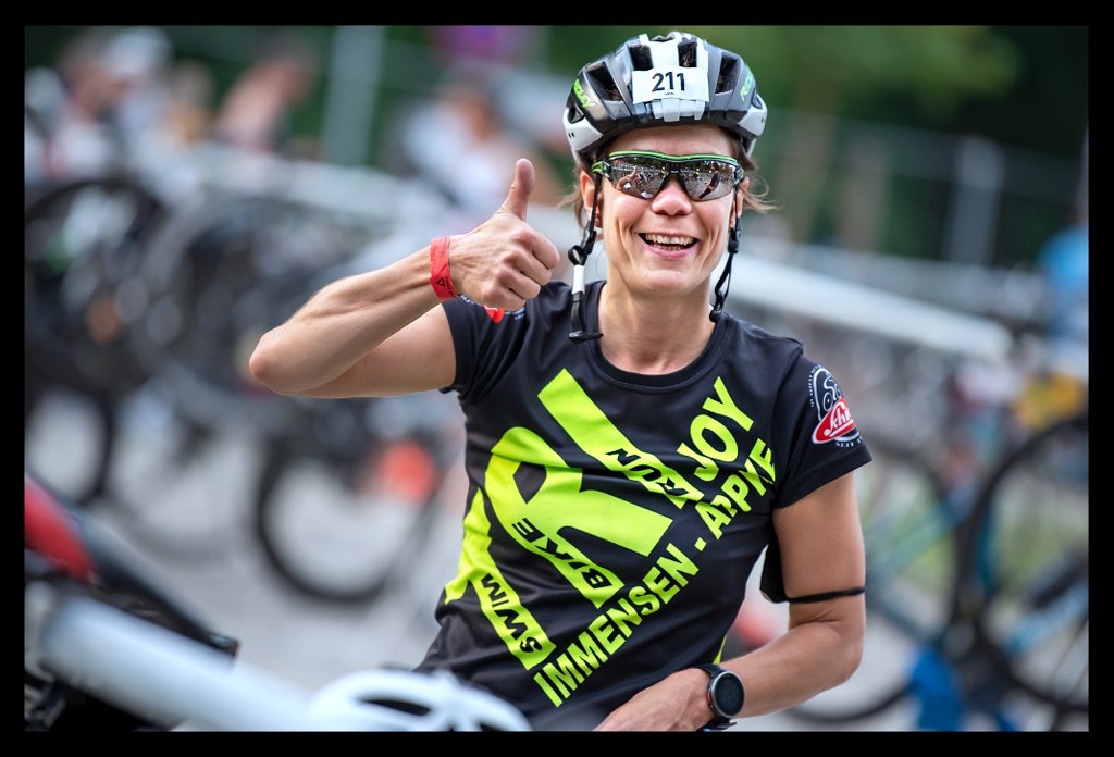 triathletin lacht daumen hoch helm sonnenbrille wechselzone bike check-in zeitfahrräder stangen city triathlon berlin strandbad wannsee die finals 2022