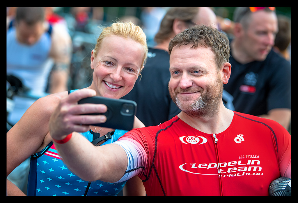 selfie bei triathlon triathlet mann roter rennanzug zeppelin team osc potsdam mit nadin eiswuerfelimschuh blauer tri-suit ale cycling wechselzone strandbad wannsee die finals 2022