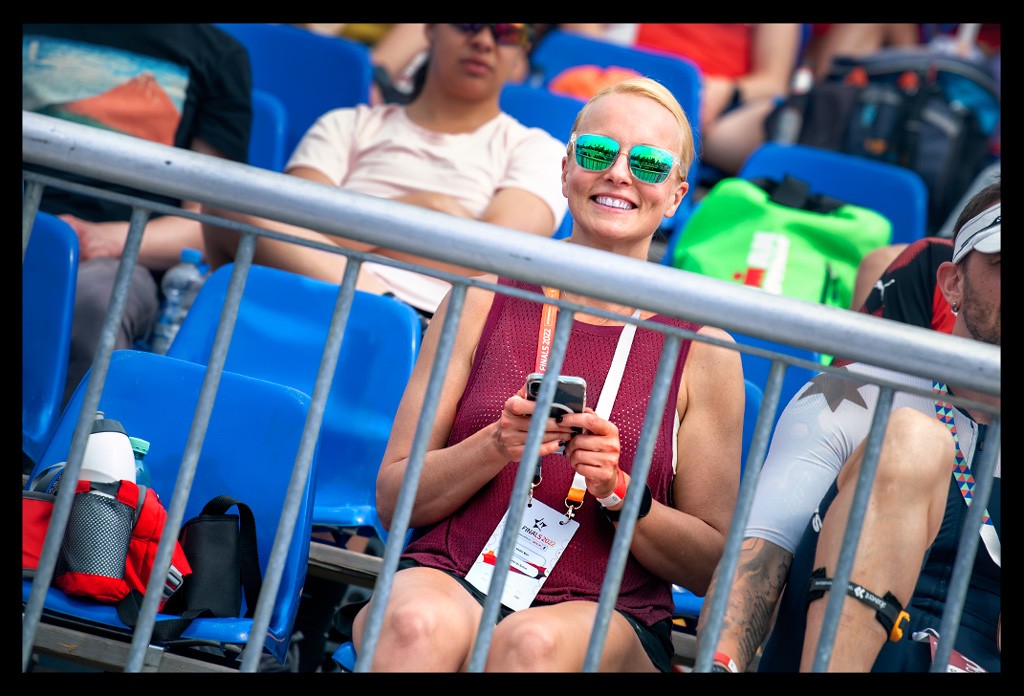 zuschauerin frau auf tribüne bei die finals berlin deutsche DTU Triathlon meisterschaften sprintdistanz elite sommerlich warm lächelt in kamera smartphone in hand sonnenbrille rotes top