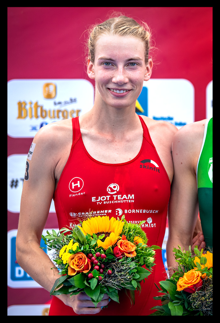 Annika Koch finals berlin deutsche DTU triathlon meisterschaft siegerehrung lächelt blumenstrauß in hand bitburger im hintergrund