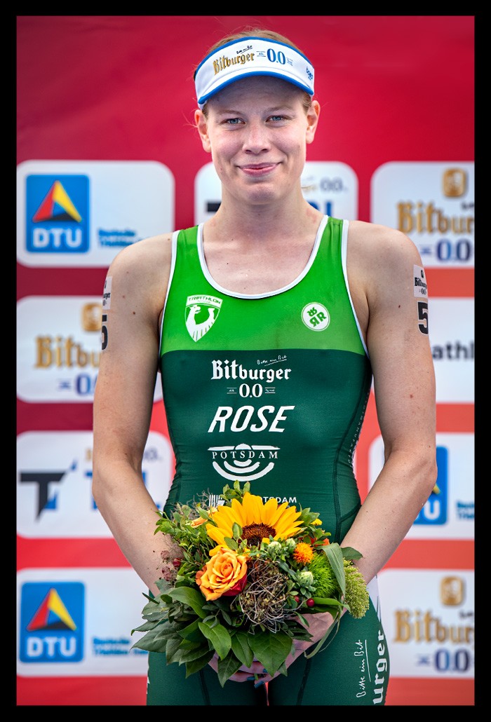 Laura Lindemann lächelt freude siegerin finals berlin deutsche DTU triathlon meisterschaft siegerehrung sprintdistanz lächelt blumenstrauß in hand grüner rennanzug Triathlon Potsdam e.V.