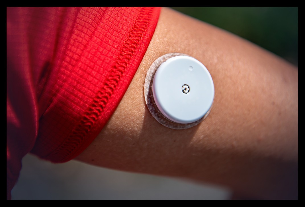 Supersapiens Glucose Biosensor abbott libre am arm nadel in haut athletin überwacht Blutzuckerwerte beim sport rechte seite rotes shirt