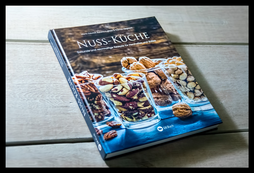 Buch "Nuss-Küche: Gesunde und reichhaltige Rezepte für Herzhaftes und Süßes" aufgeschlagen auf weißem Holzschreibtisch liegend