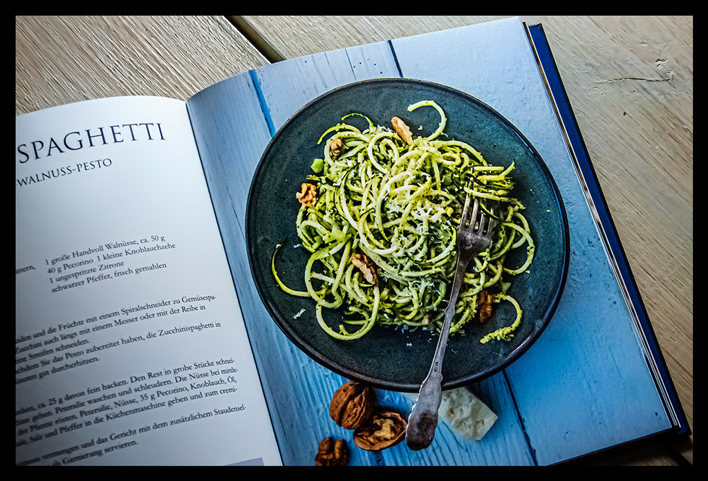 Buch "Nuss-Küche: Gesunde und reichhaltige Rezepte für Herzhaftes und Süßes" aufgeschlagen mit Foto von Znoodles auf weißem Holzschreibtisch liegend