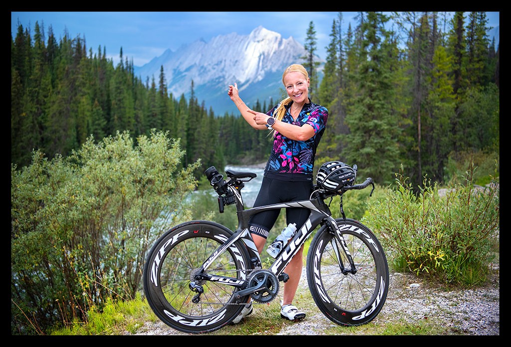 Radsportlerin steht vor Berg Landschaft Kanada Rocky Mountains testet Garmin EDGE 1040 Solar GPS-Fahrradcomputer und lächelt