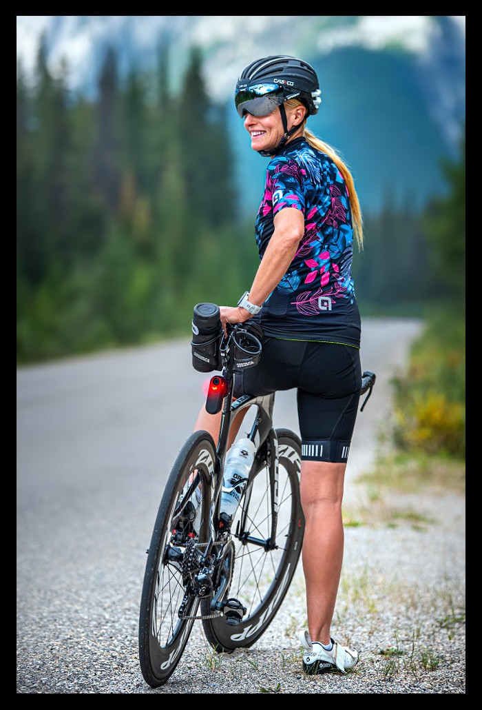Radsportlerin mit Garmin VARIA Bike Radar RCT716 Rücklicht mit Kamera steht strasse in kanada endlose weite Berge Landschaft autoverkehr sicherheit lächelt testet gerät