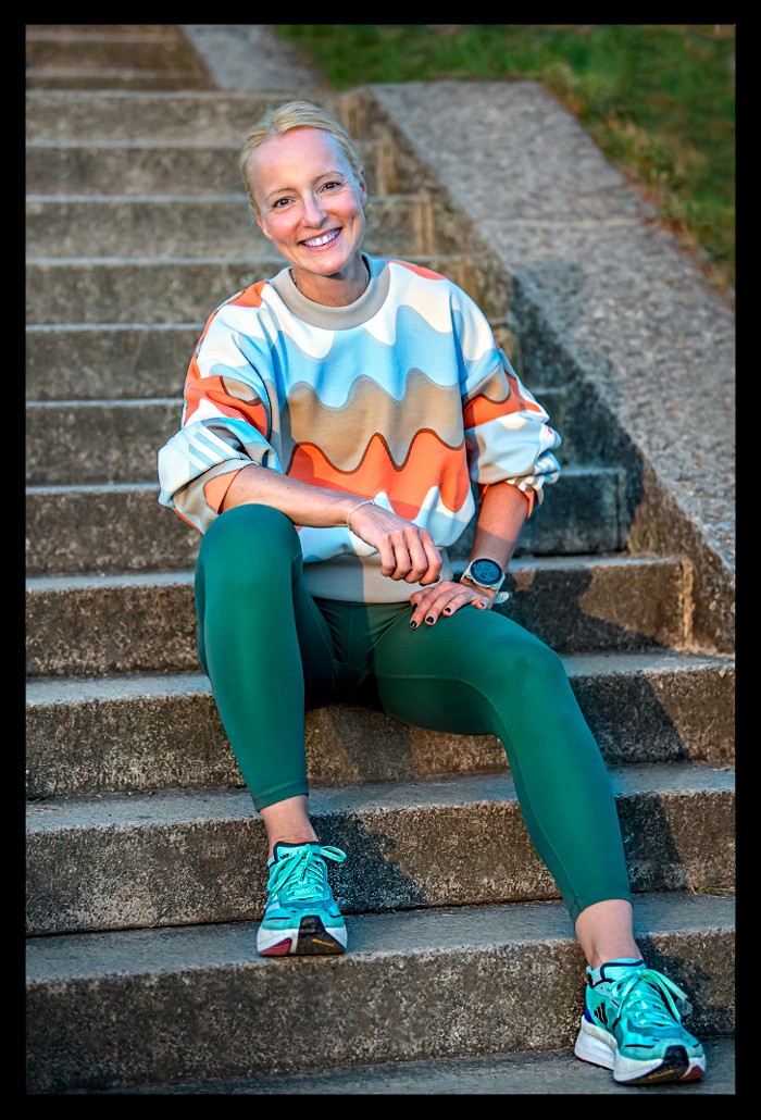Laufbloggerin Nadin alias Eiswuerfelimschuh auf Treppe sitzend lachend mit Adidas Laufschuh, grüner Lauftights und buntem Pullover