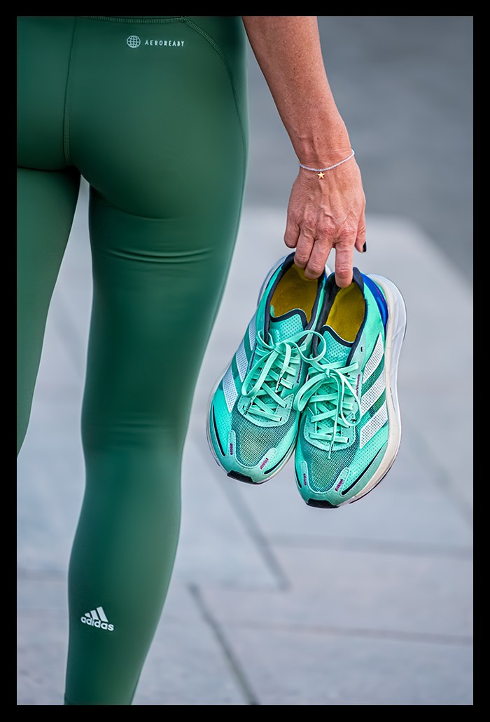 Laufbloggerin Nadin alias Eiswuerfelimschuh stehend nur Beine zu sehen mit Adidas Laufschuh in Hand und grüner Lauftights 