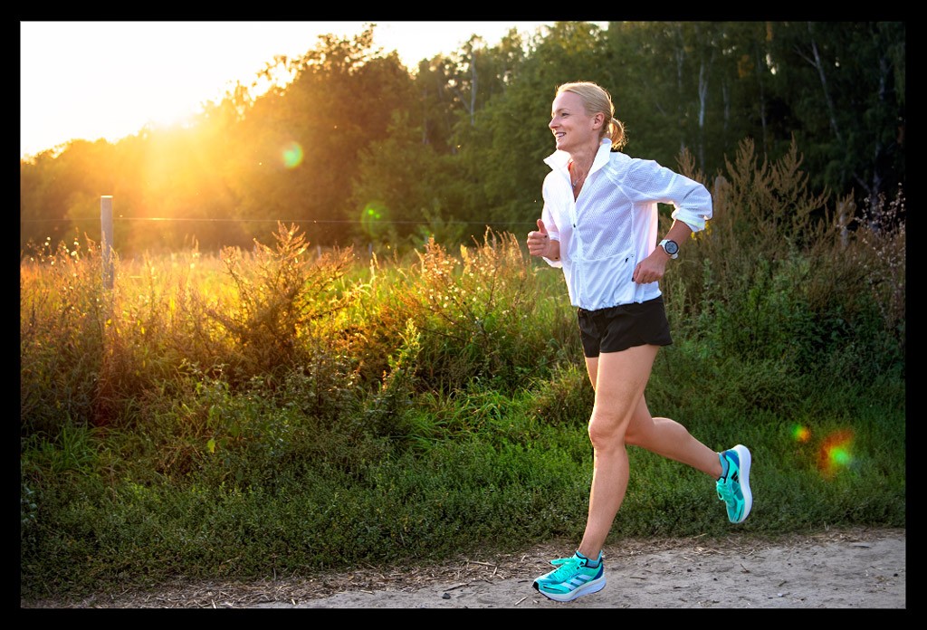 Triathletin und Laufbloggerin Nadin vor grüner Landschaft und Sonnenuntergang laufend mit Adidas Laufschuhen und Outfit und Garmin Forerunner 955 Solar