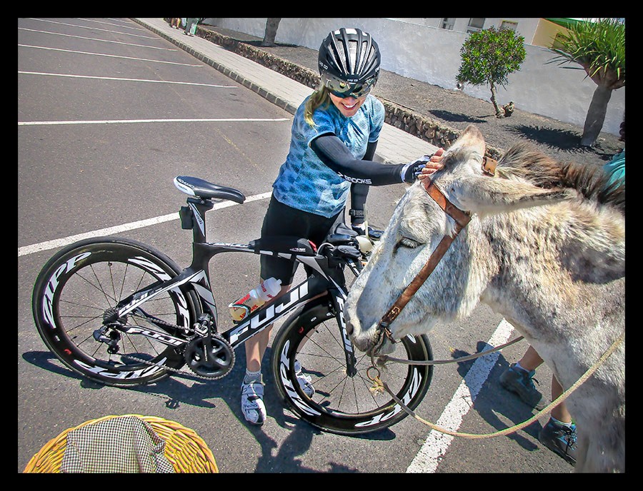 Frau mit Triathlonrad auf Lanzarote Kanaren streichelt einen Esel bei einer trainingspause