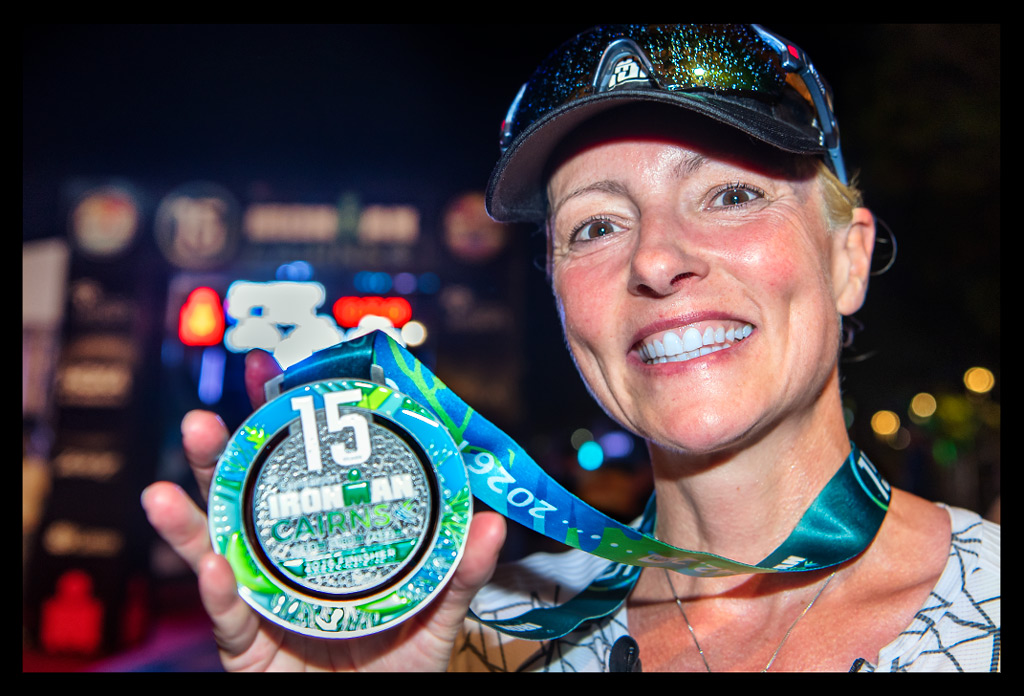Ironman Cairns 2026 - Finisher Medaille mit einer lächelnden Athletin mit Visor und Sportsonnenbrille auf Ziellinie