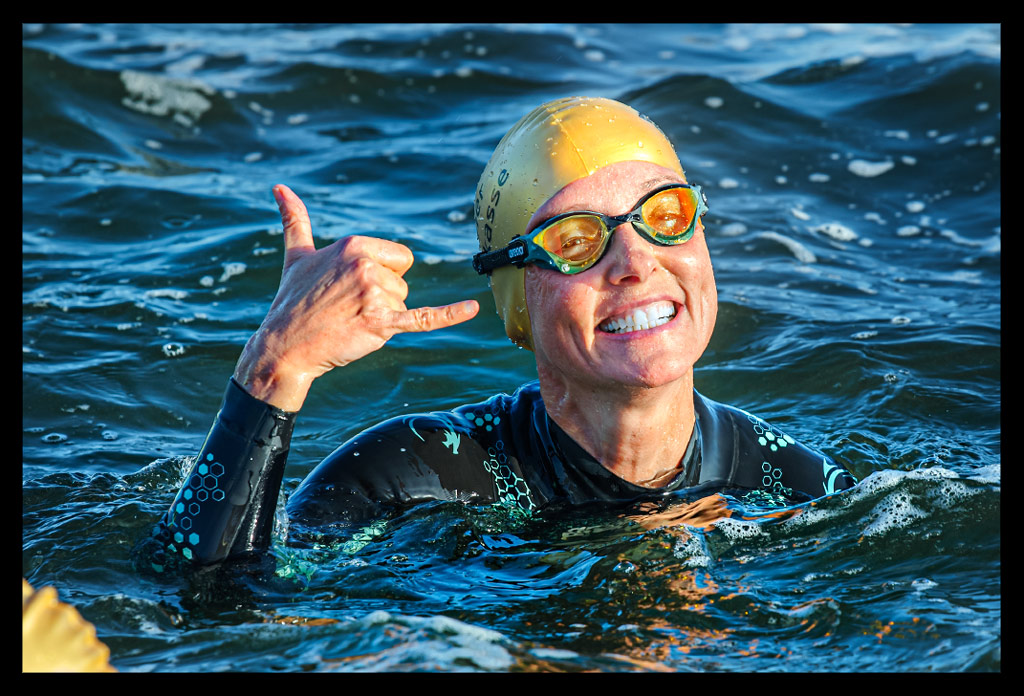 Triathletin Nadin von eiswuerfelimschuh.de lächelnd im Wannsee schwimmend mit und Neoprenanzug an und goldener Jubiläums-Badekappe