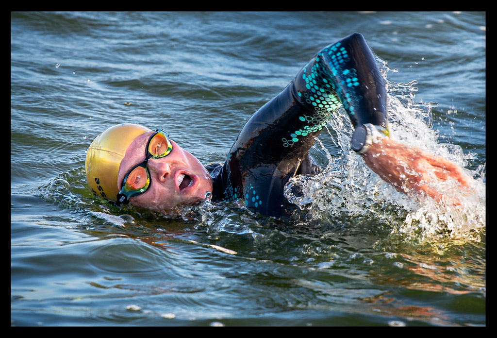 Triathletin Nadin von eiswuerfelimschuh.de lächelnd im Wannsee kraulend schwimmend mit und Neoprenanzug an und goldener Jubiläums-Badekappe