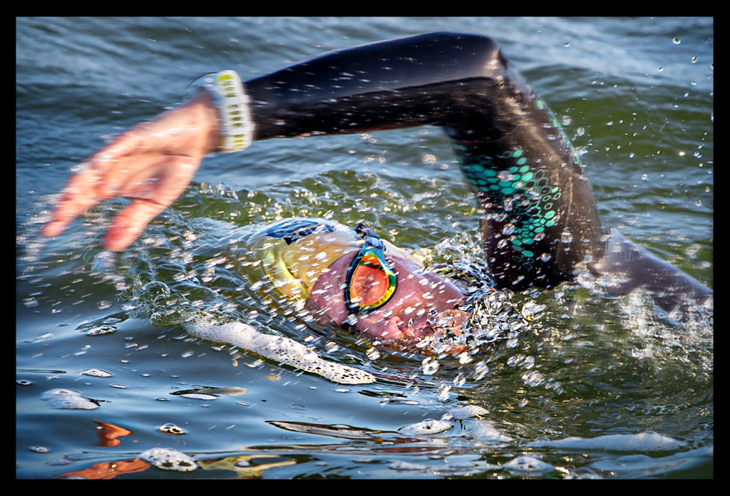 Triathletin Nadin von eiswuerfelimschuh.de lächelnd im Wannsee kraulend schwimmend mit und Neoprenanzug an und goldener Jubiläums-Badekappe