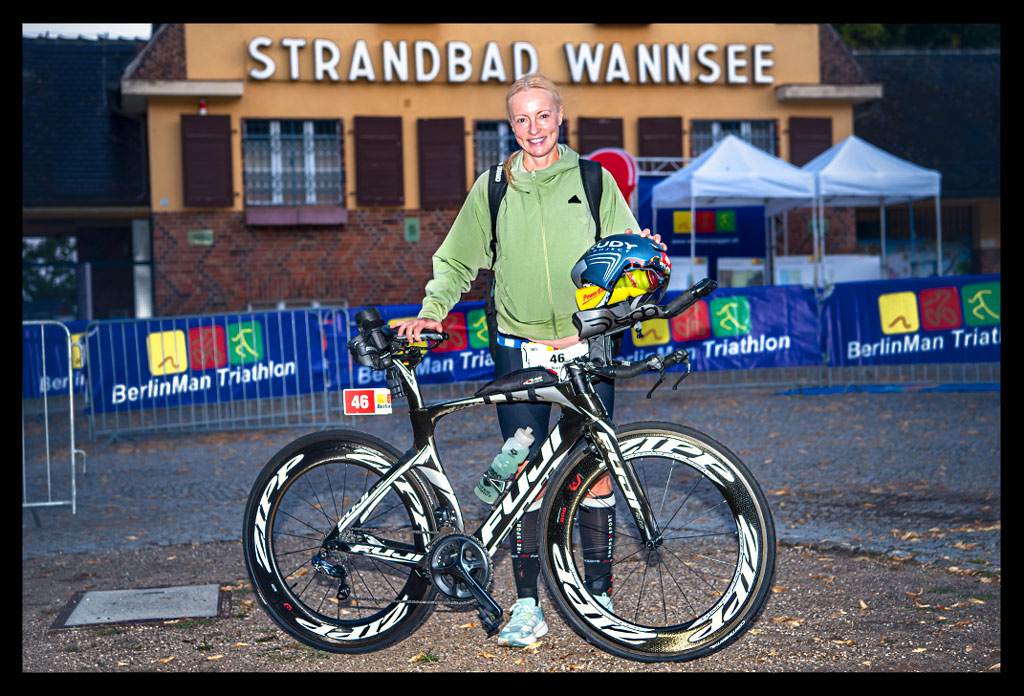 Triathlon vor dem Strandbad Wannsee Hauptgebäude und BerlinWoMan-Triathlon Bannern mit ihrem Zeitfahrrad und Zeitfahrhelm in der Hand