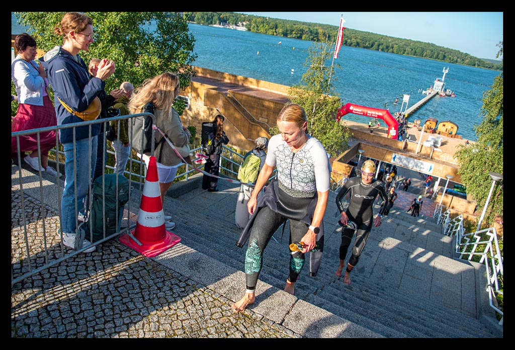 Triathletin Nadin von eiswuerfelimschuh.de nach Schwimmstrecke beim BerlinWoMan-Triathlon die Treppenstufen am Strandbad Wannsee hoch laufend mit Neoprenanzug an und goldener Jubiläums-Badekappe
