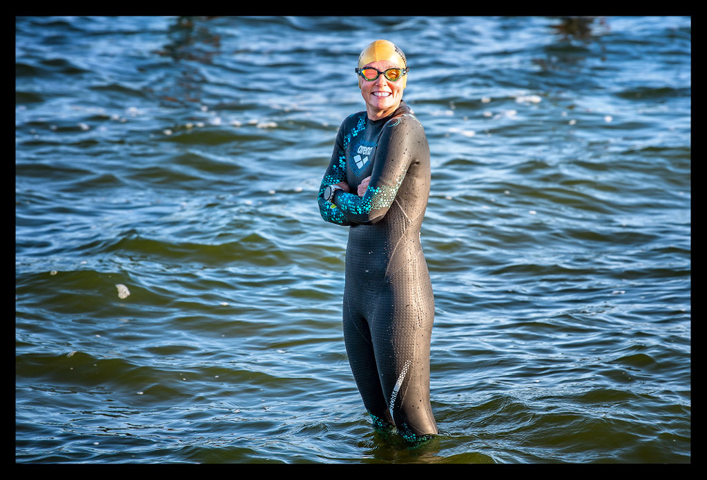 Triathletin Nadin von eiswuerfelimschuh.de lächelnd am Strandbad Wannsee im Wasser stehend mit und Neoprenanzug an und goldener Jubiläums-Badekappe